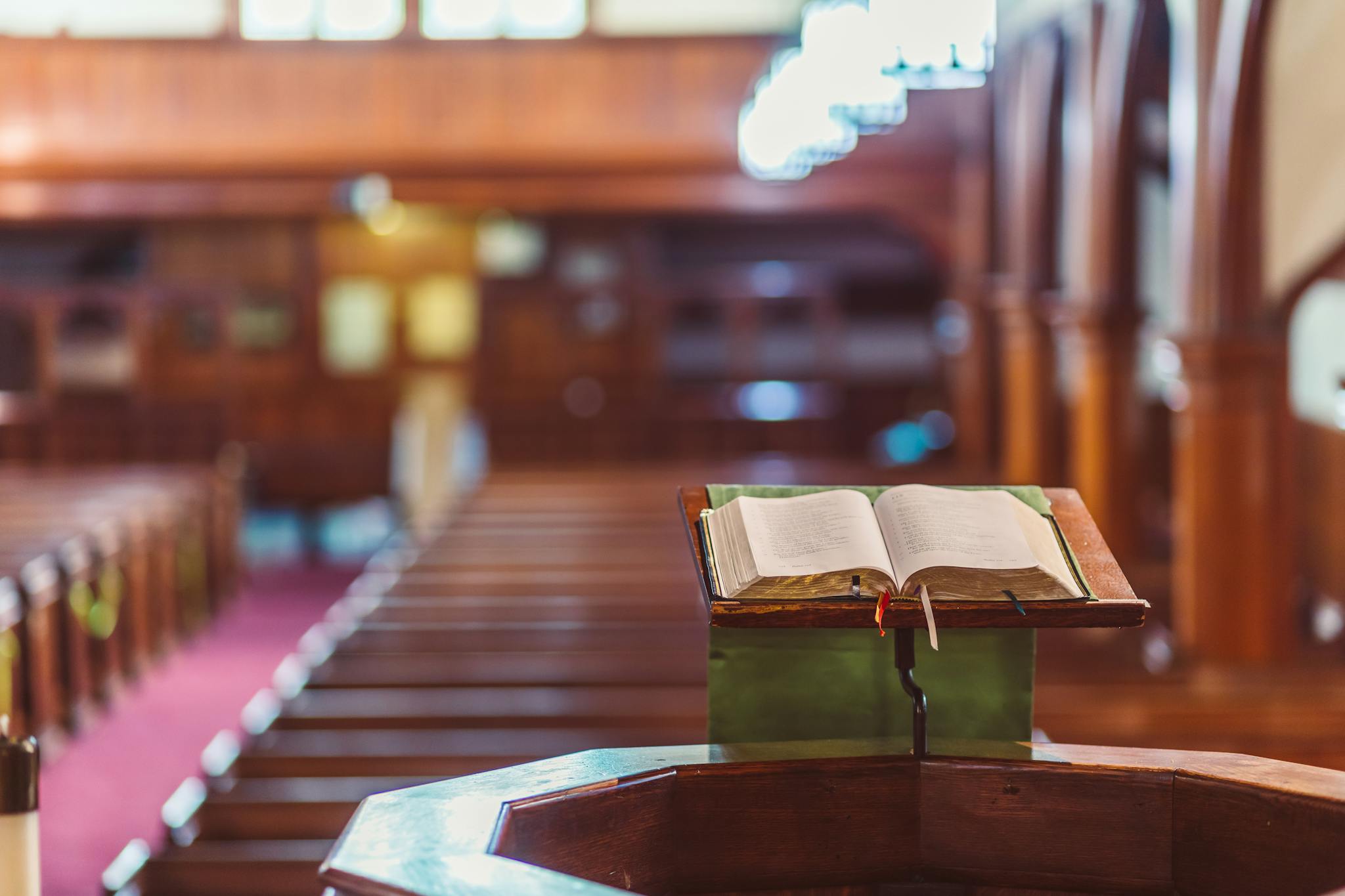 Open Bible on a wooden pulpit in a serene church setting with blurred pews in the background.